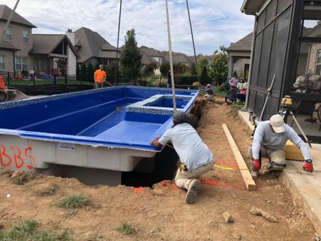 Workers place a fiberglass pool mold into the ground